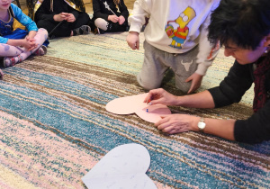 Chłopiec przy pomocy pani Ewy przebija papierowe serce