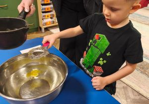 Chłopiec trzyma klucz nad miską podczas lania wosku