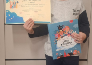 Chłopiec stoi i pokazuje dyplom i nagrodę