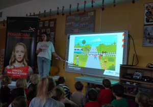 Prowadząca pokazuje na tablicy, czego nie wolno robić przy przejazdach kolejowych