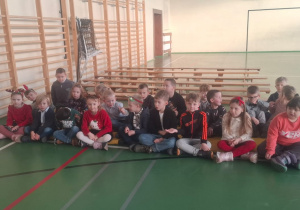 Dzieci siedzą w sali gimnastycznej