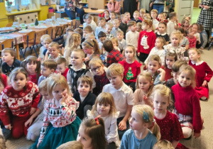 Dzieci siedzą na dywanie i oglądają występy kolegów