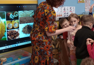 Pani Asia podaje dzieciom do wąchania ziarna kakaowca w słoiku