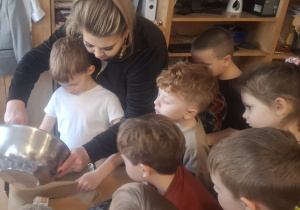 Chłopiec przy pomocy Pani Kasi przekłąda masę do formy