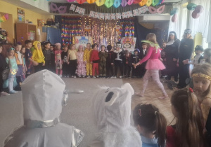 Dzieci stoją w kole, a w środku chodzi wodzirejka