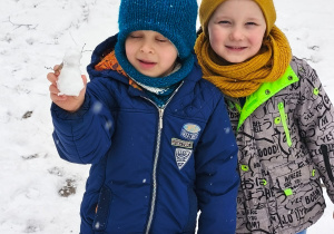 Dwóch chłopców, a jeden z nich trzyma w dłoni ulepionego bałwanka