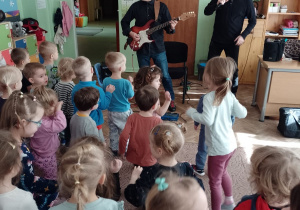 Muzyk gra na gitarze, pan Witek stoi z mikrofonem, a dzieci poruszają się do muzyki