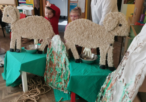 Dwoje dzieci stoi przy sylwetach owiec