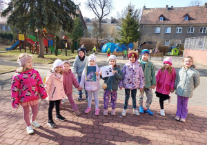 Kilkoro dzieci stoi, a dwoje z nich trzyma zdjęcie wilka i jego ślady