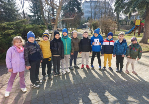 Kilkoro dzieci stoi, a jeden chłopiec trzyma zdjęcie śladów zwierzęcia