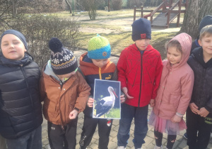 Kilkoro dzieci stoi, a jeden chłopiec trzyma zdjęcie bociana