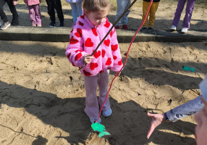 Dziewczynka łowi sylwetę ryby w piaskownicy