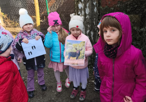 Kilkoro dzieci stoi, a dwoje trzyma zdjęcia zwierzęcia i jego ślady