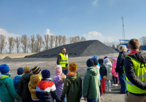 dzieci stoją przed hałdą węgla, a pracownik opowiada dzieciom