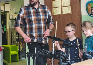 Muzyk stoi przy perkusji, a chłopiec trzyma pałeczki i gra