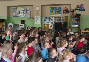 Dzieci siedzą na dywanie i klaszczą w dłonie