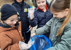 Kilkoro dzieci wrzuca odpady do worka