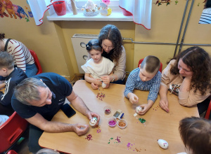 Dzieci z rodzicami przy stoliku ozdabiają jajka