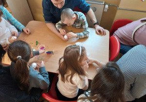Dzieci z rodzicami przy stoliku ozdabiają jajka