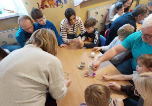 Dzieci z rodzicami przy stoliku ozdabiają jajka