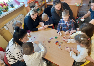 Dzieci z rodzicami przy stoliku ozdabiają jajka