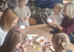 Kilkoro dzieci z rodzicami przy stoliku ozdabiają jajka