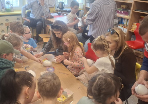 Kilkoro dzieci z rodzicami przy stoliku ozdabiają jajka