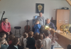 Chłopiec gra na ustniku, obok stoi dwóch nauczycieli szkoły