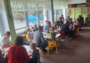 Rodzice z dziećmi przy stolikach ozdabiają jajka