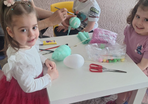 Troje dzieci z panią Wiesią ozdabiają jajka