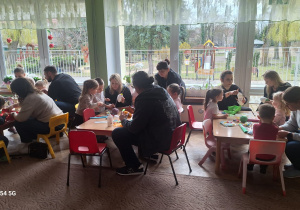 Rodzice z dziećmi przy stolikach ozdabiają jajka