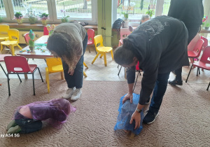 Dwka dzieci skulone na dywnie nakryte chustką przez rodziców