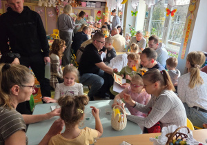 Dzieci z rodzicami przy stolikach malują zajączki