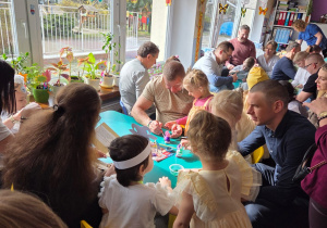 Kilkoro dzieci z rodzicami przy stoliku malują zajączki