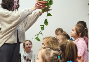 Pani bibliotekarka pokazuje dzieciom doniczkę z rośliną