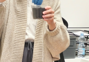 Pani bibliotekarka wsadza roślinkę do pojemniczka z ziemią