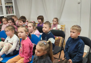 Dzieci siedzą w czytelni i słuchają opowiadania