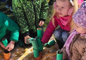 Kilkoro dzieci tworzy drzewa z rolek po papierze