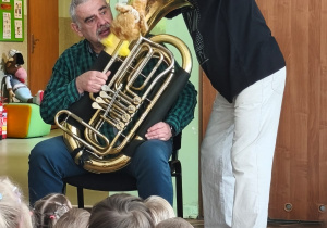 Muzyk trzyma instrument, a prowadzący objasnia wygląd