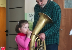 Dziewczynka gra na instrumencie, który trzyma muzyk