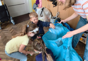 Prowadząca trzyma worek, a kilkoro dzieci wrzuca śmieci