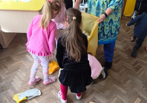 Prowadząca trzyma worek, a kilkoro dzieci wrzuca śmieci