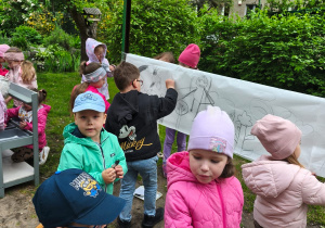 Dzieci rysują węglem na rozwieszonym kartonie
