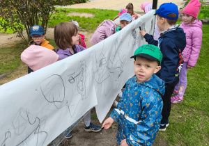 Dzieci rysują węglem na rozwieszonym kartonie