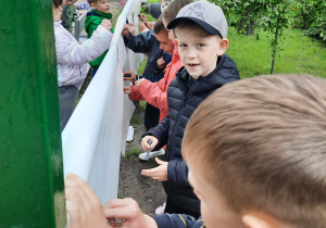 Dzieci rysują węglem na rozwieszonym kartonie