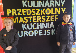dwoje dzieci stoi przy napisie - Przegląd Kulinarny "Przedszkoly Masterszef"