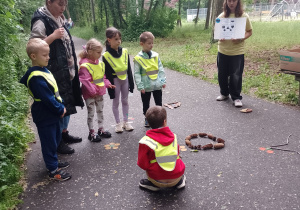 Dzieci z panią i wolontariuszką przy stacji w układanie figur z darów przyrody