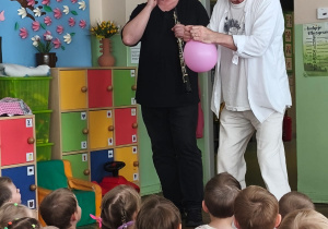 Muzyk trzyma obój, a pan Witek nadmuchany balon