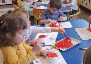 Dzieci przy stołach malują miseczki na muchomory