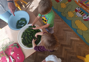 Dwoje dzieci wyciąga ogórki z miski